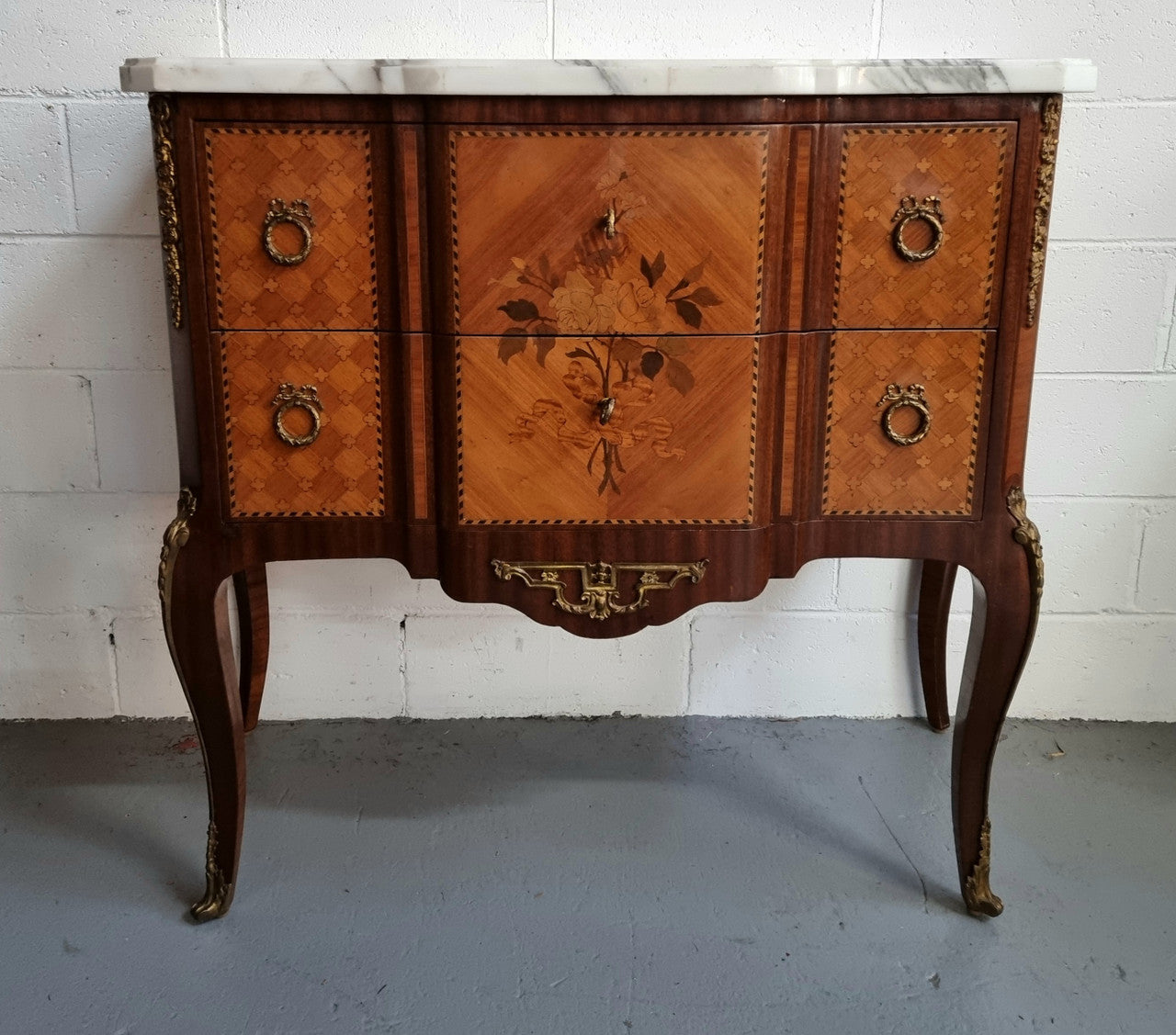 Lovely French Louis XV/XVI style Transitional marquetry inlaid commode. There are two drawers and beautiful ormolu mounts with a nice marble top in good original detailed condition.