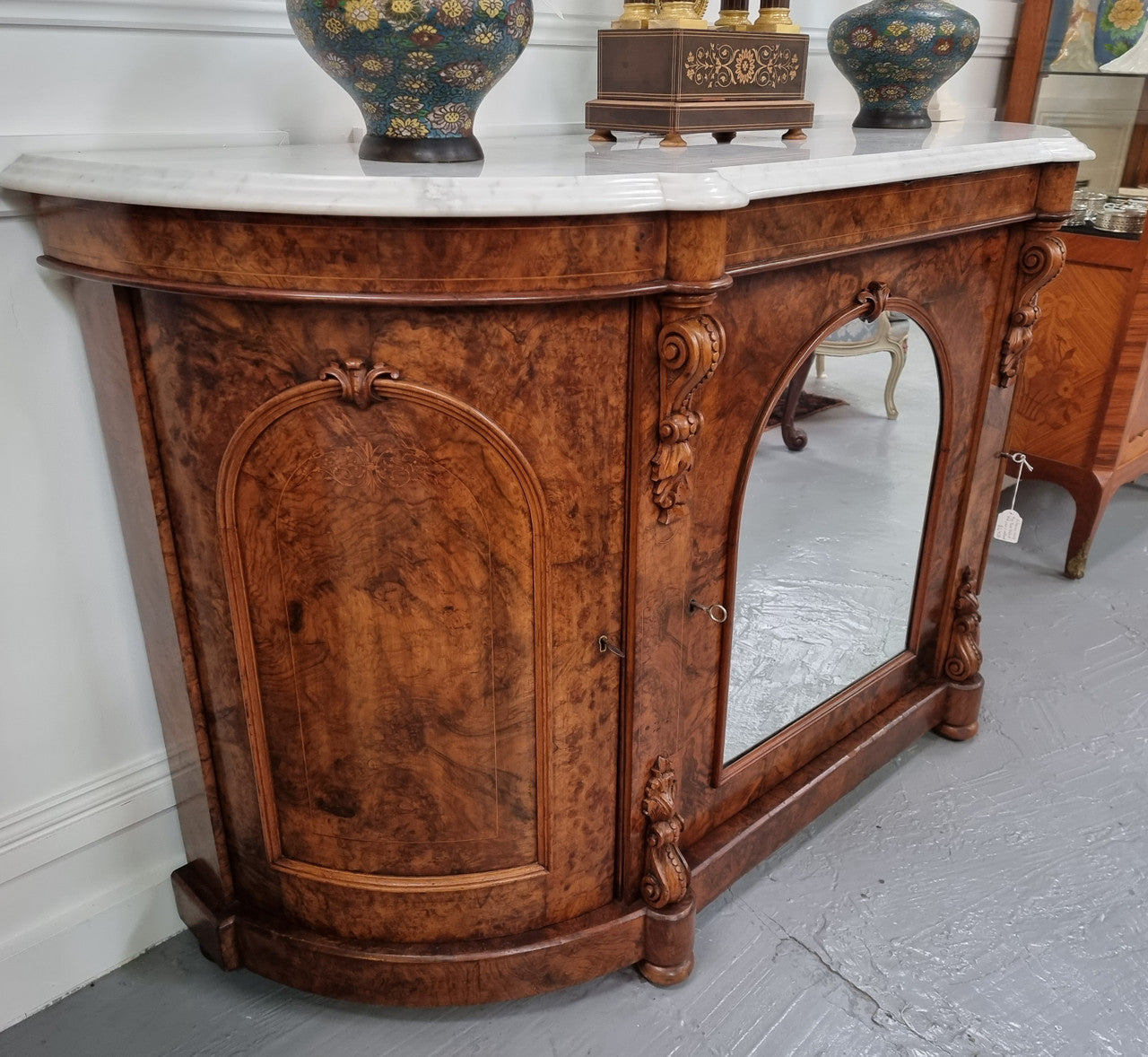An elegant Antique Victorian Burr wood Walnut marble-top sideboard credenza with a mirrored center door. It has a white shaped marble top, mirror front, nicely carved details and three swing doors along with two keys. It is in good original detailed condition.