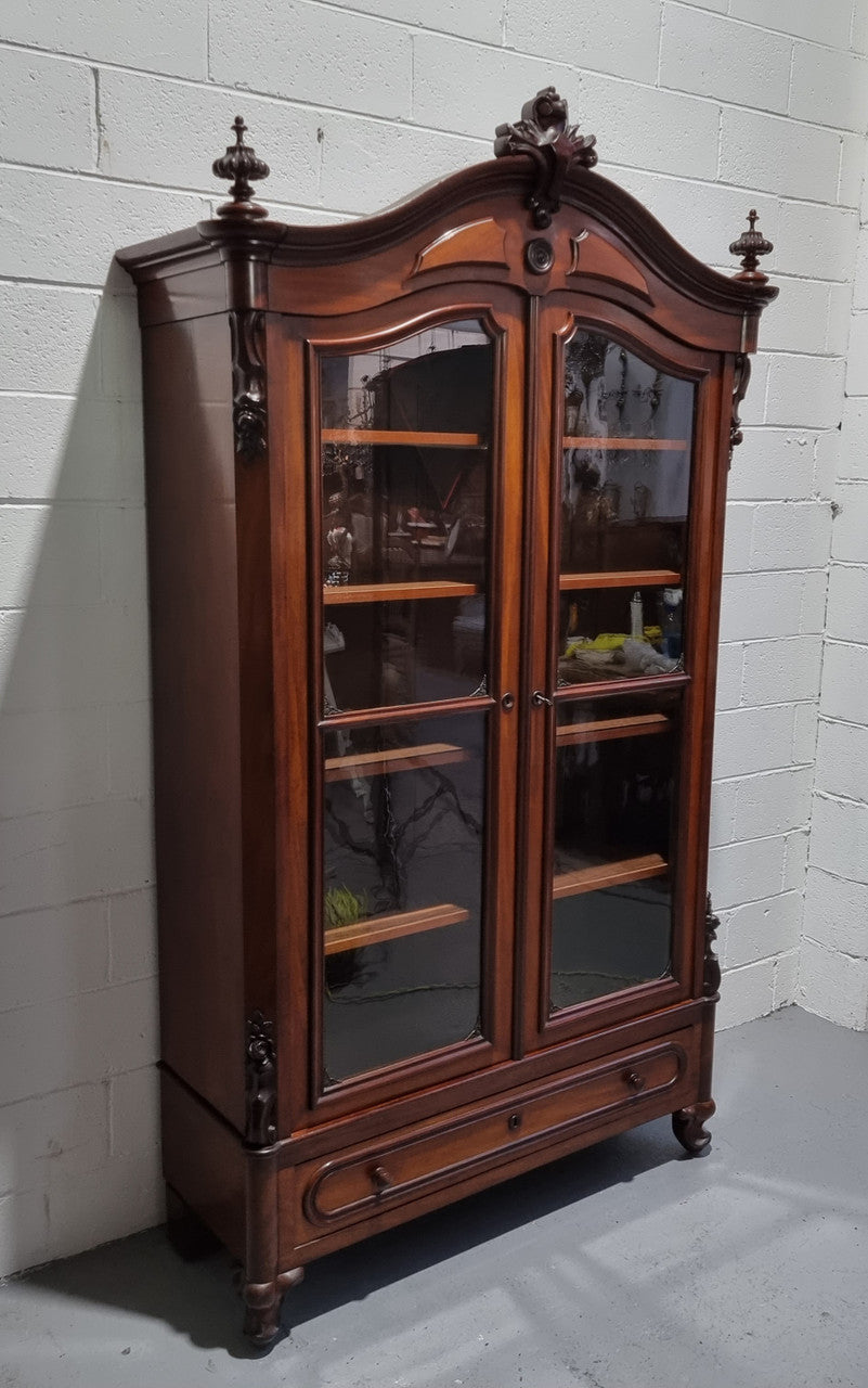 Antique Mahogany two door Biedermeier style bookcase with four fully adjustable shelves and a drawer at the bottom. The two wooden finials at the top are easily removed for a different look of desired. In good original detailed condition.