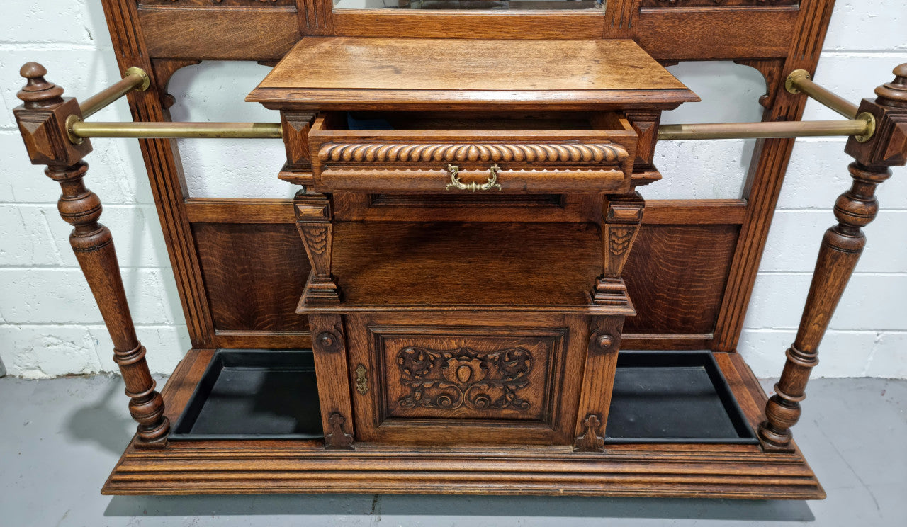 Grand Henry 2nd Style French Oak hall stand with 12 hanging hooks. Also has one cupboard and drawer for storage along with a mirror and two areas either side for umbrellas and walking sticks. In good original detailed condition.