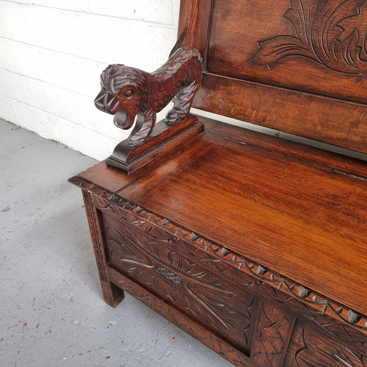 Unusual English Oak Monks Bench. The tabletop is set onto a lift top chest in such a way that when the table is not in use, the top pivots to a vertical position and becomes the back of a Settle. Carved Lion table rests and carving to front. In good, detailed condition.