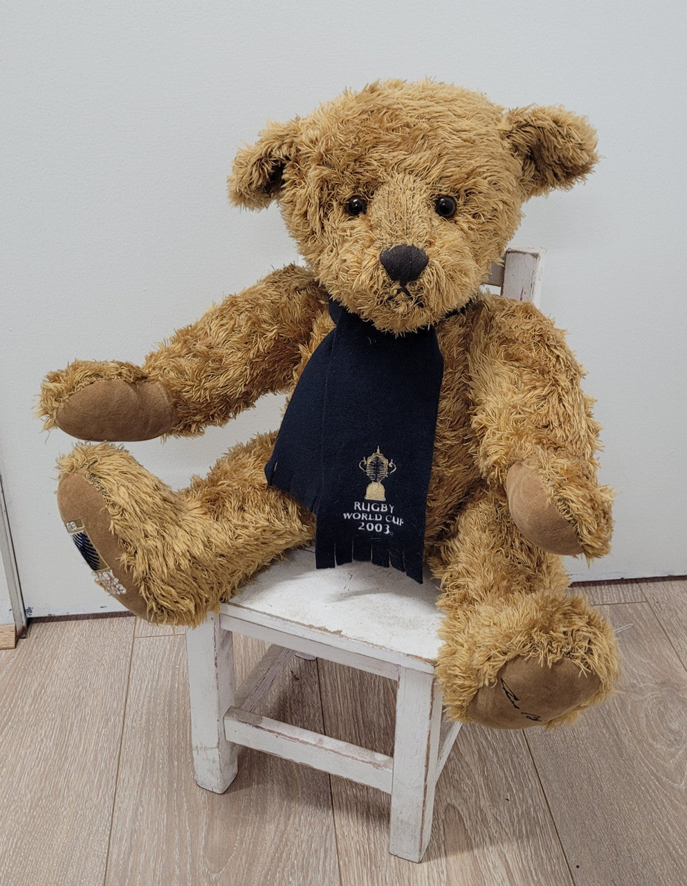 World Cup Rugby Bear. William by RUSS a special release for 2003. Limited to 5000 pieces worldwide. 50.8 cm fully jointed golden-brown bear with suedeen paw pads and blue scarf with Rugby World Cup Logo embroidery.
*Please note chair in photo is not included.