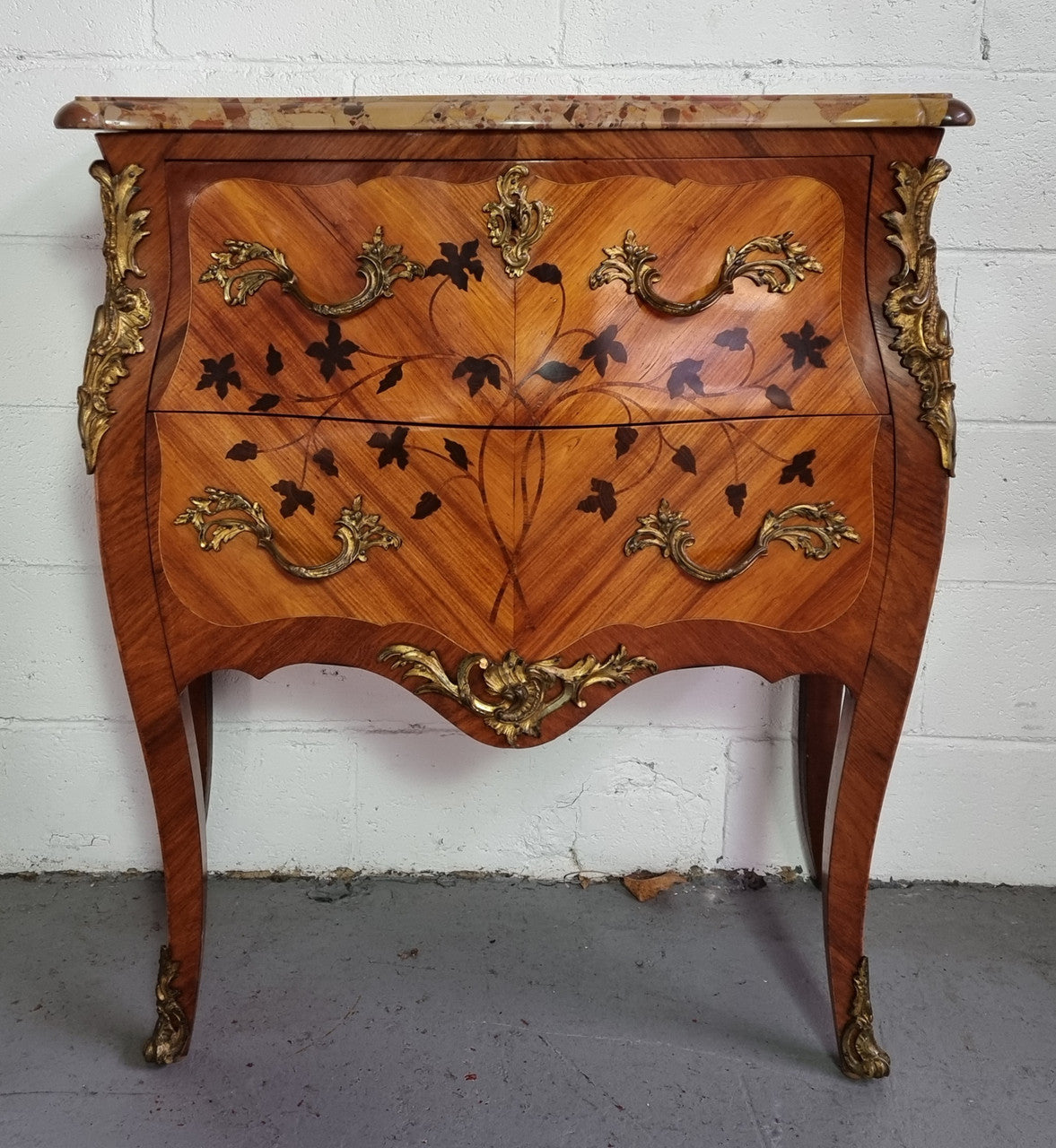 Charming petite French Louis XV style commode featuring two drawers, marquetry inlay, ormolu trim and marble Top. In good original detailed condition. Circa: 1930’s.