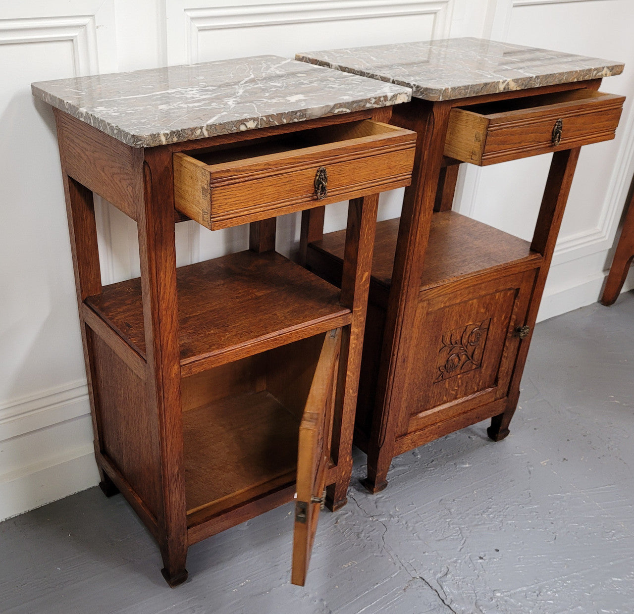 Pair of French Oak Arts & Crafts style marble top bedside cabinets. They have lovely carvings on the door, an open shelf in the middle and drawer at the top. They are in good original detailed condition.