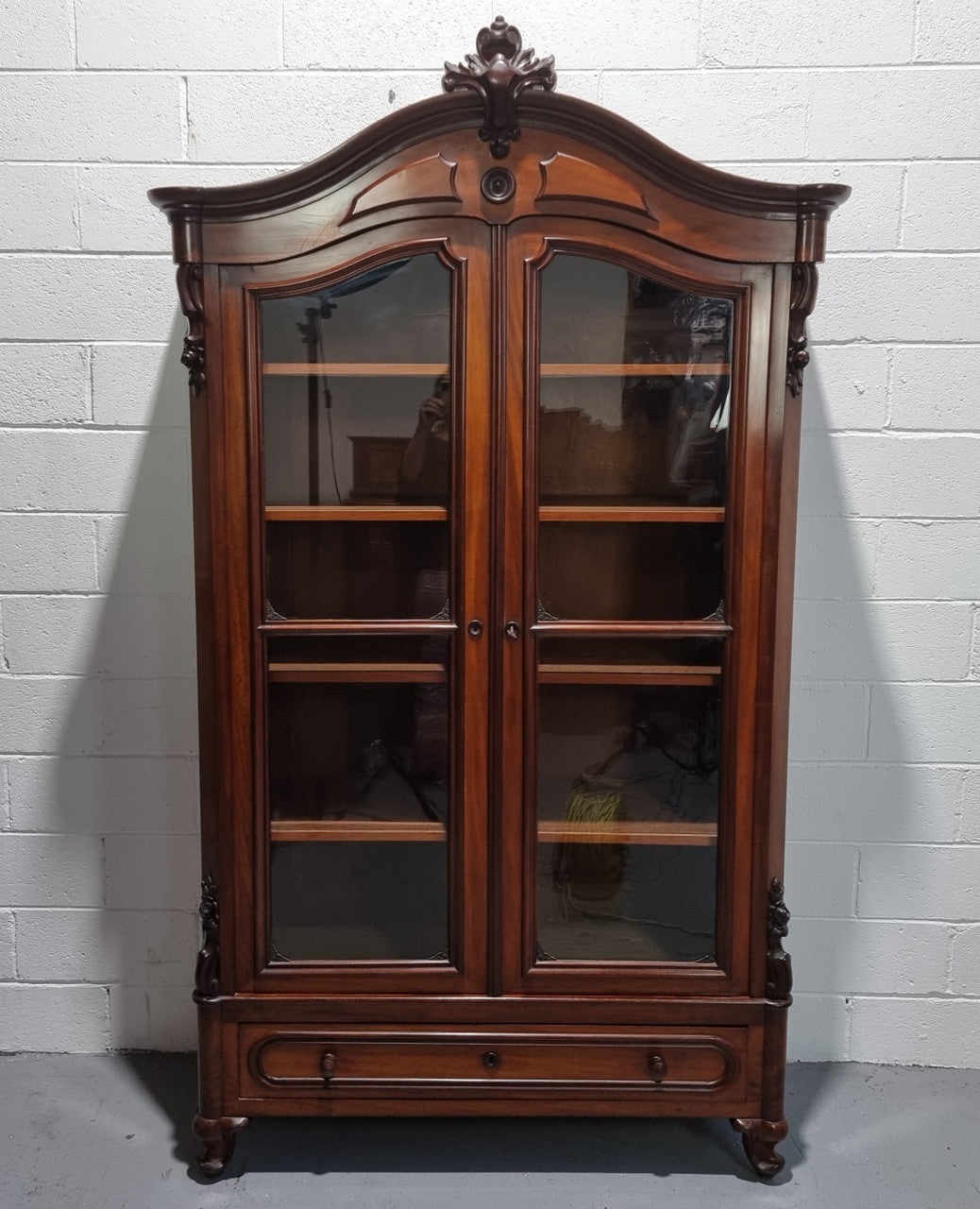 Antique Mahogany two door Biedermeier style bookcase with four fully adjustable shelves and a drawer at the bottom. The two wooden finials at the top are easily removed for a different look of desired. In good original detailed condition.