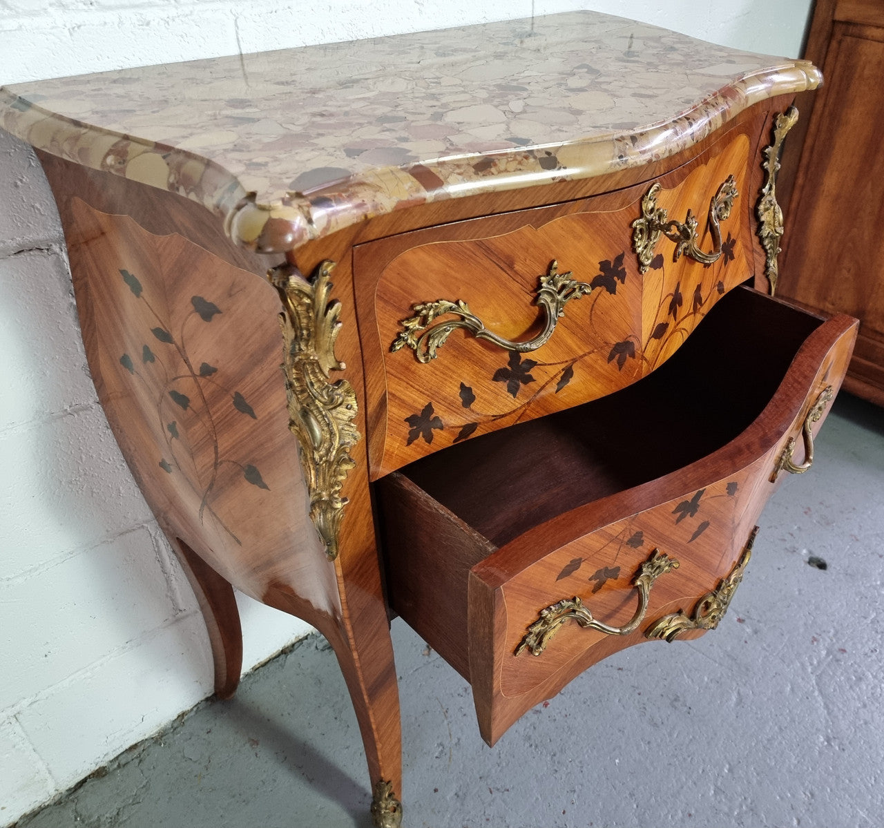 Charming petite French Louis XV style commode featuring two drawers, marquetry inlay, ormolu trim and marble Top. In good original detailed condition. Circa: 1930’s.