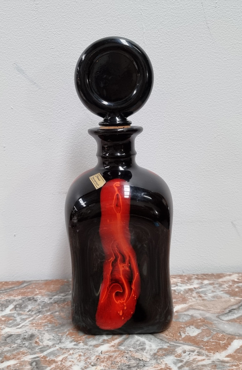 Vintage Designer glass carafe by “Stromit Handarbeit”. Dark background with flashes of orange/red.