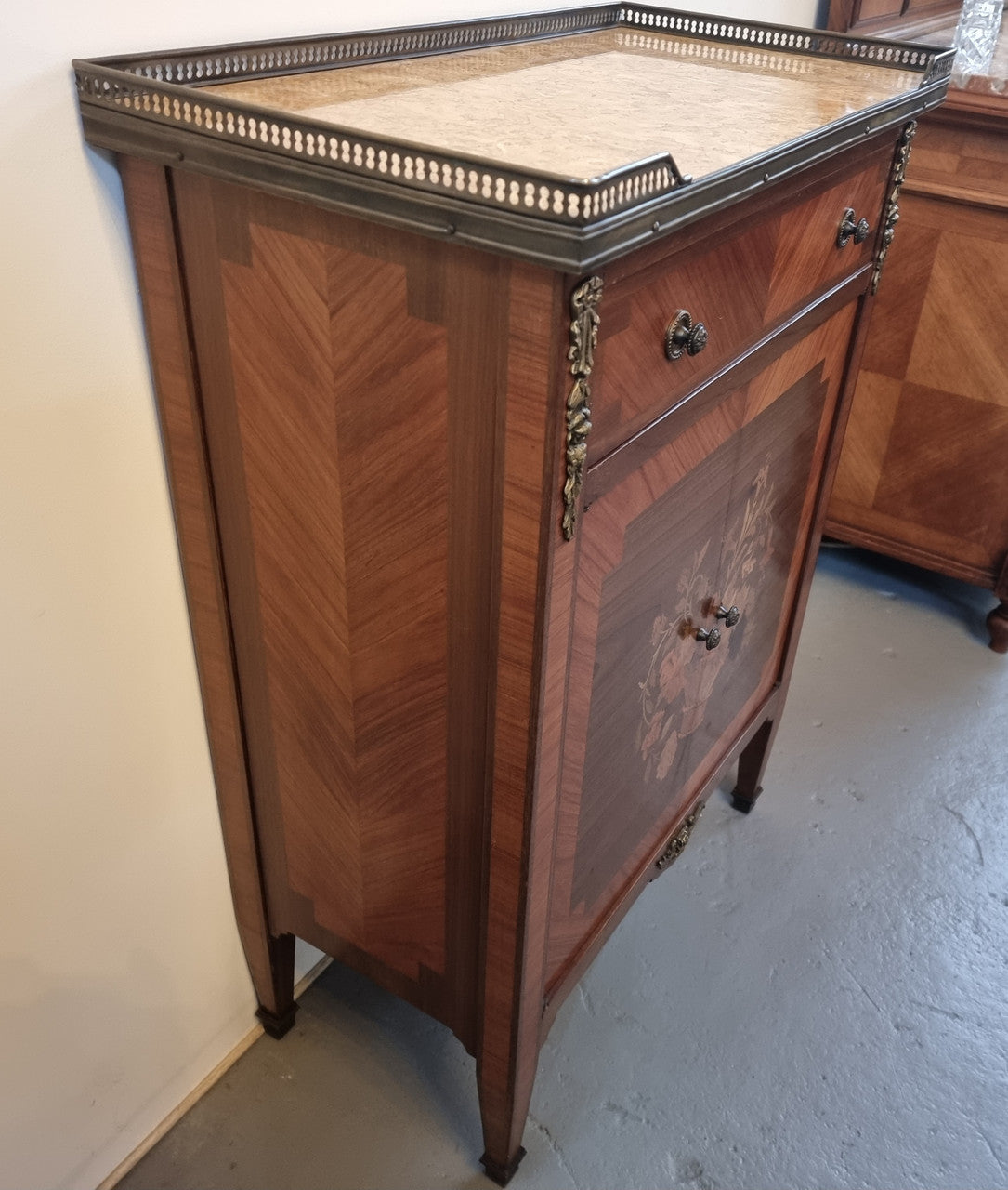 Louis 16th style marquetry inlaid side cabinet with a pierced brass gallery surrounding a marble top. It has two doors open up to storage with one shelf and a drawer above that. In good original detailed condition.