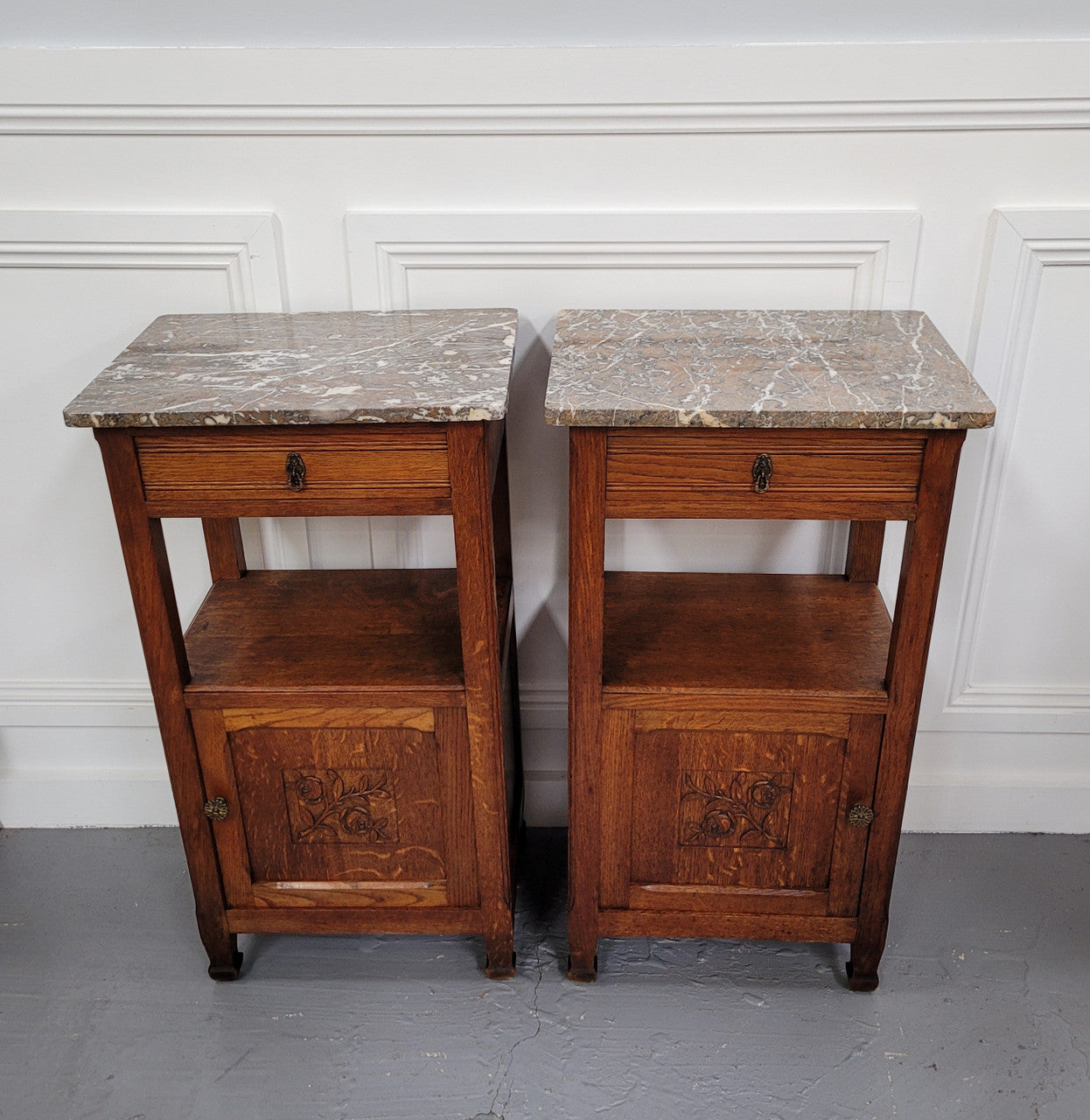 Pair of French Oak Arts & Crafts style marble top bedside cabinets. They have lovely carvings on the door, an open shelf in the middle and drawer at the top. They are in good original detailed condition.