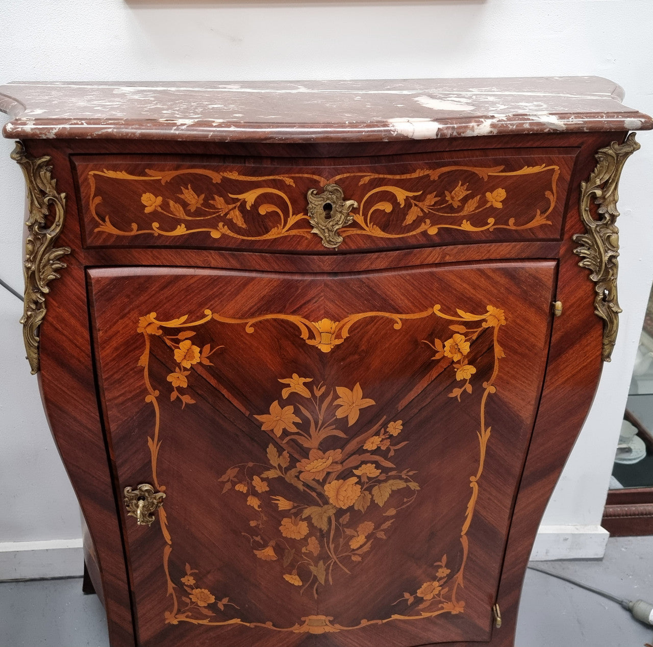 Stunning French Transitional style Mahogany marquetry inlay salon cabinet in the bombe shape. It has one draw, one shelf, marble top & ormolu decoration. Sourced from France and in good original detailed condition.