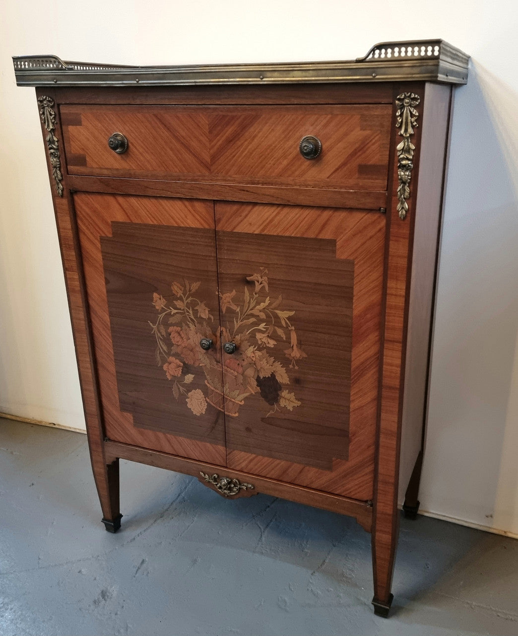 Louis 16th style marquetry inlaid side cabinet with a pierced brass gallery surrounding a marble top. It has two doors open up to storage with one shelf and a drawer above that. In good original detailed condition.