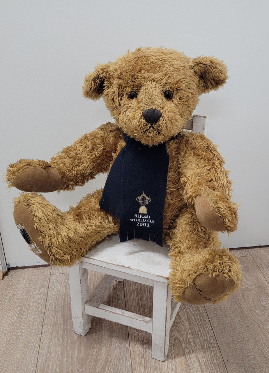 World Cup Rugby Bear. William by RUSS a special release for 2003. Limited to 5000 pieces worldwide. 50.8 cm fully jointed golden-brown bear with suedeen paw pads and blue scarf with Rugby World Cup Logo embroidery.
*Please note chair in photo is not included.