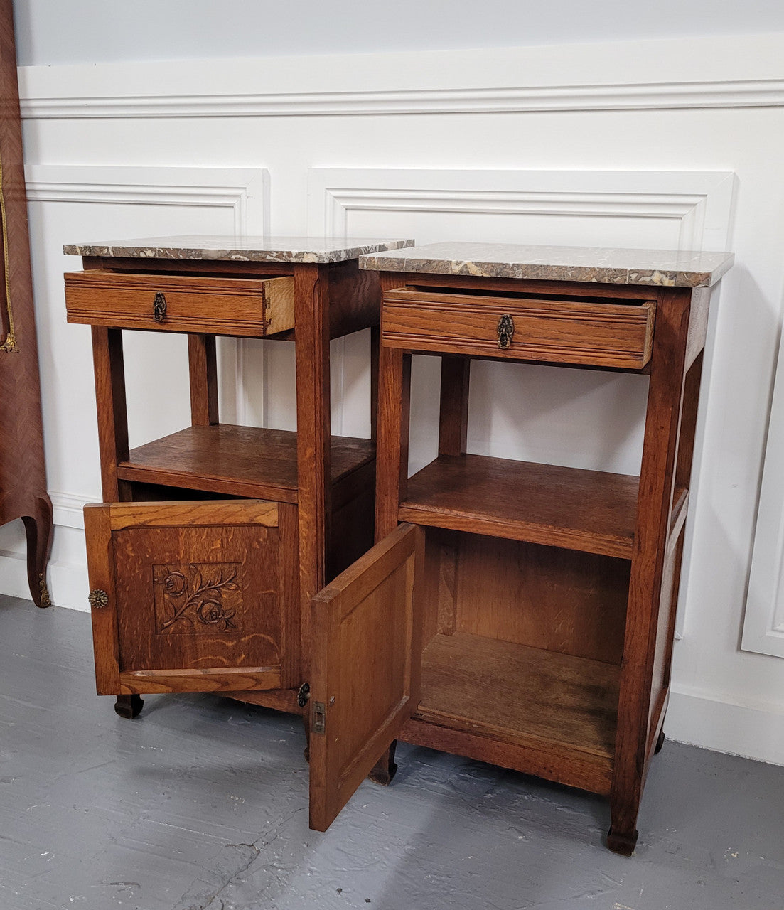 Pair of French Oak Arts & Crafts style marble top bedside cabinets. They have lovely carvings on the door, an open shelf in the middle and drawer at the top. They are in good original detailed condition.