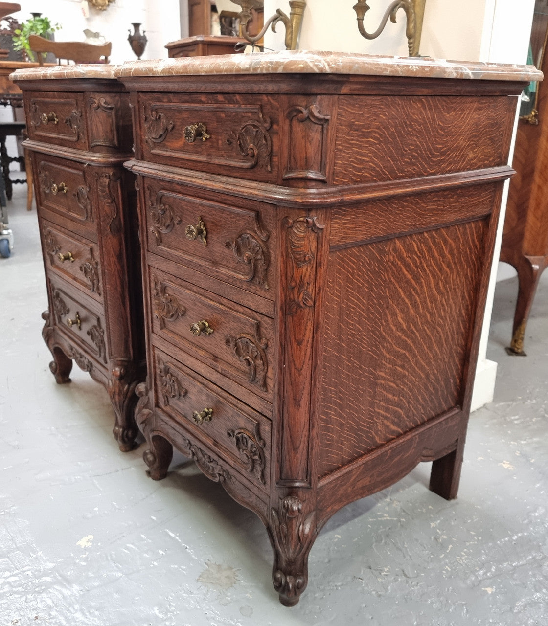 A pair of hard to find French Oak Louis XV style four drawer marble topped bedsides with attractive carvings. They are in good original detailed condition and have been sourced from France.