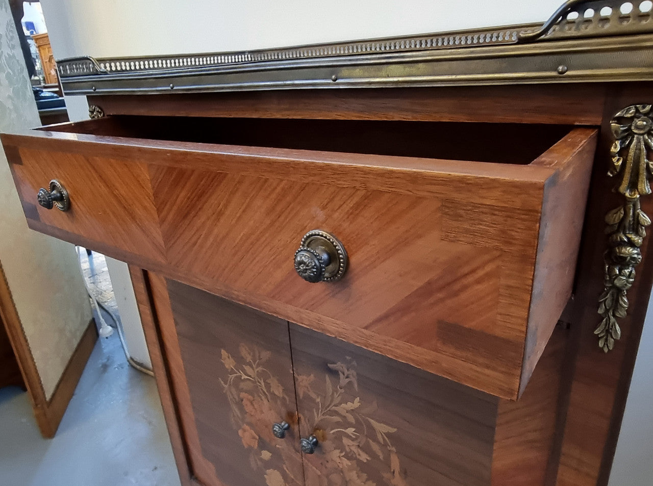 Louis 16th style marquetry inlaid side cabinet with a pierced brass gallery surrounding a marble top. It has two doors open up to storage with one shelf and a drawer above that. In good original detailed condition.