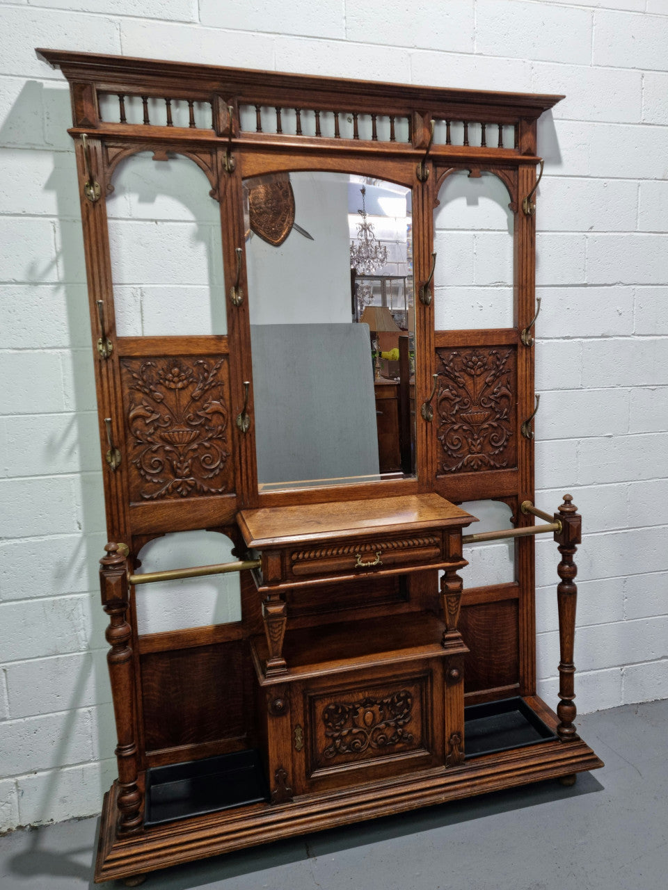 Grand Henry 2nd Style French Oak hall stand with 12 hanging hooks. Also has one cupboard and drawer for storage along with a mirror and two areas either side for umbrellas and walking sticks. In good original detailed condition.