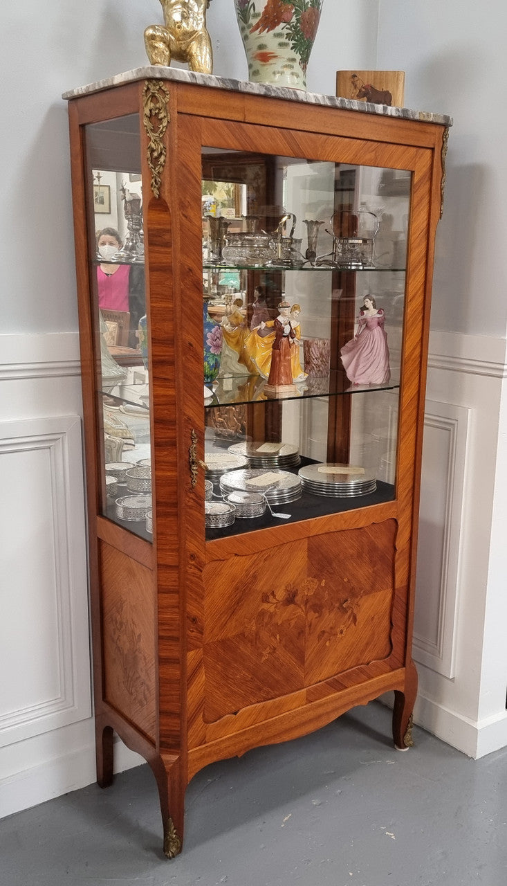 Beautiful French walnut inlaid vitrine with a lovely marquetry design and ormolu mounts. Has a beautiful coloured marble top and two glass shelves. In good original condition.