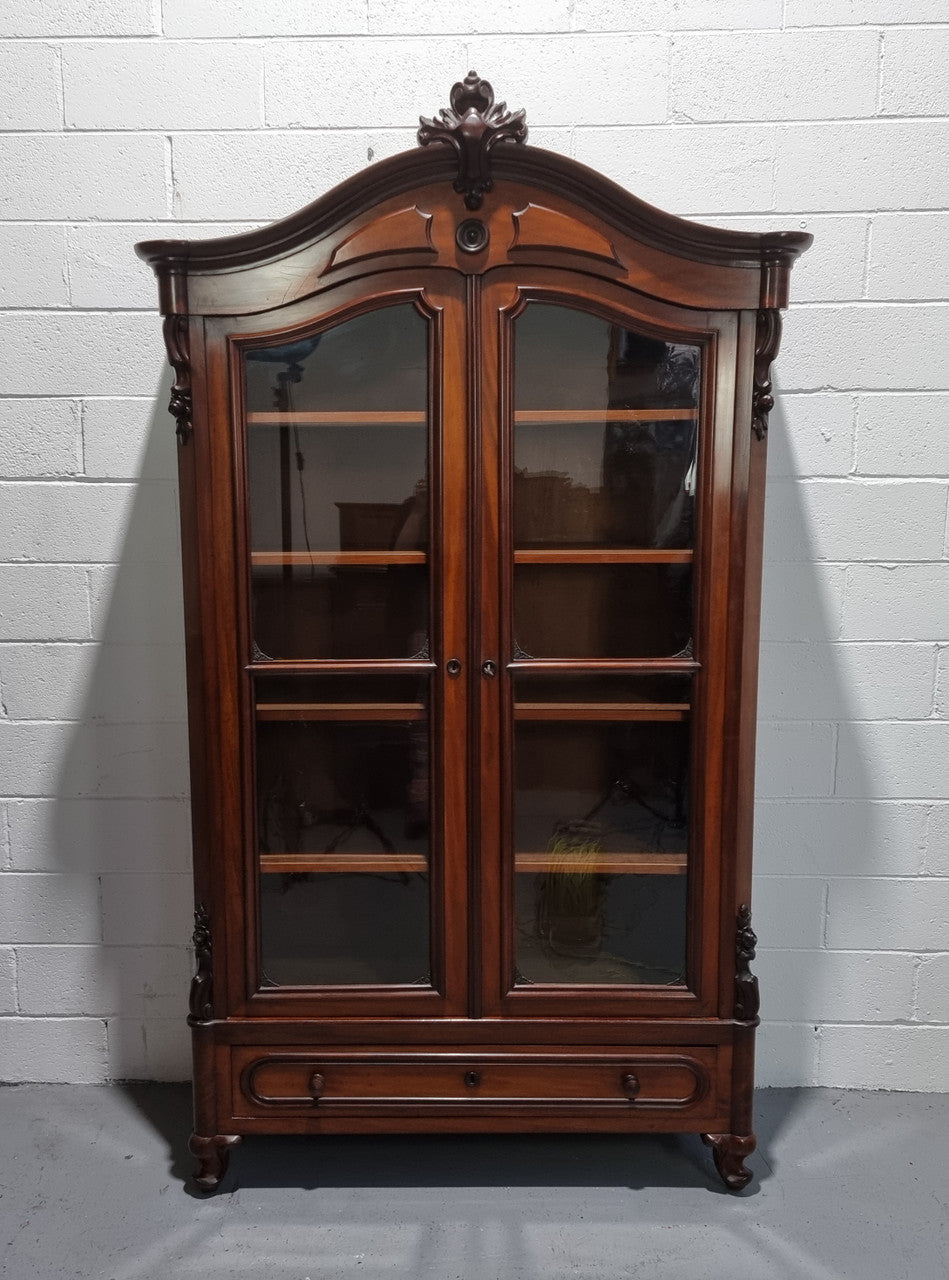 Antique Mahogany two door Biedermeier style bookcase with four fully adjustable shelves and a drawer at the bottom. The two wooden finials at the top are easily removed for a different look of desired. In good original detailed condition.