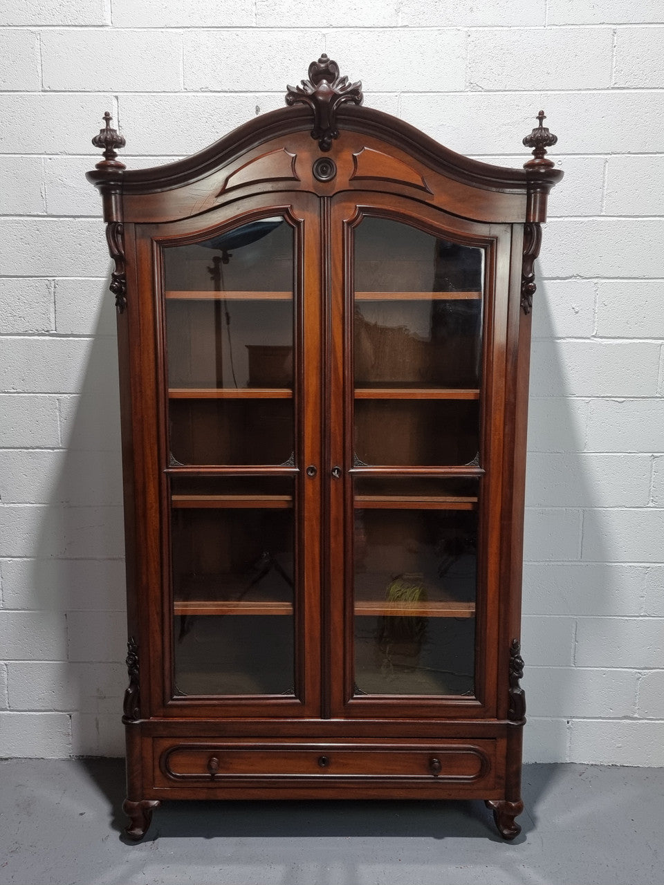 Antique Mahogany two door Biedermeier style bookcase with four fully adjustable shelves and a drawer at the bottom. The two wooden finials at the top are easily removed for a different look of desired. In good original detailed condition.