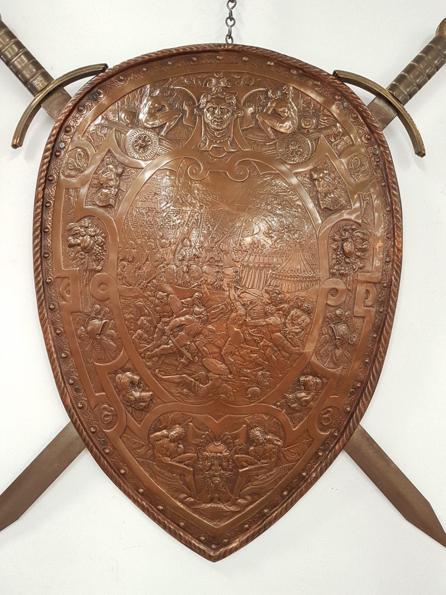 A beautiful European antique repousse copper shield, depicting a battle scene and with metal swords. It has been sourced from France and is in good original condition.