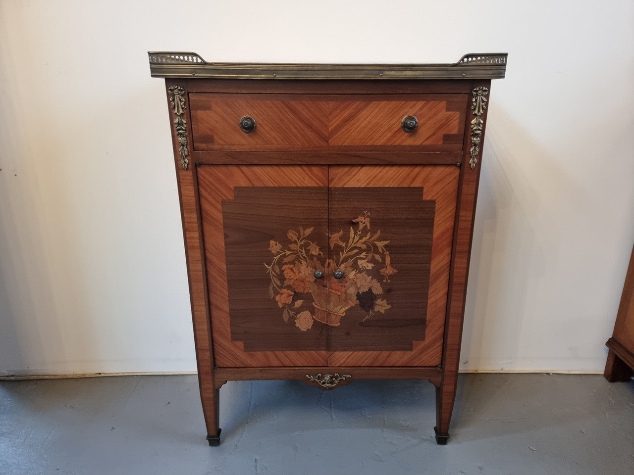 Louis 16th style marquetry inlaid side cabinet with a pierced brass gallery surrounding a marble top. It has two doors open up to storage with one shelf and a drawer above that. In good original detailed condition.