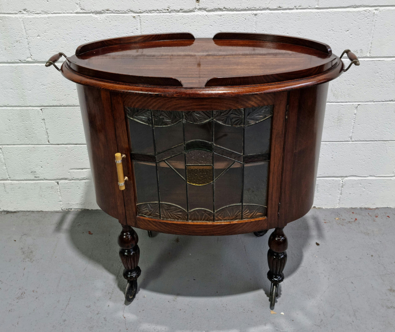 Oak Tudor auto trolley with beautiful leadlight glass. It is on wheels and the door open up to a cabinet with one shelf. In good original detailed condition.