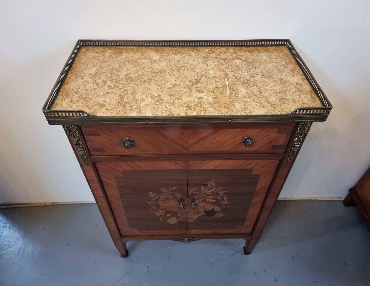 Louis 16th style marquetry inlaid side cabinet with a pierced brass gallery surrounding a marble top. It has two doors open up to storage with one shelf and a drawer above that. In good original detailed condition.
