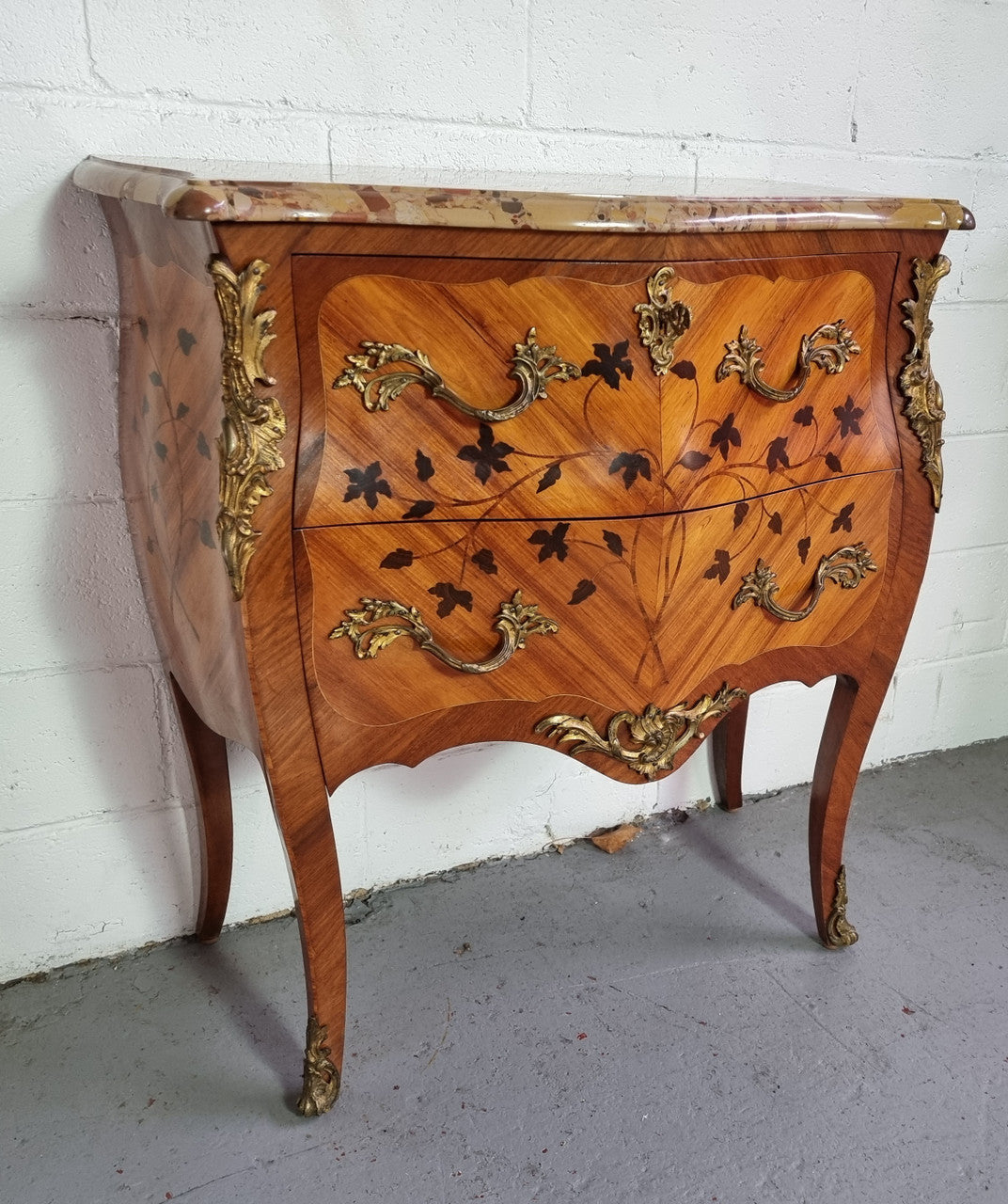 Charming petite French Louis XV style commode featuring two drawers, marquetry inlay, ormolu trim and marble Top. In good original detailed condition. Circa: 1930’s.