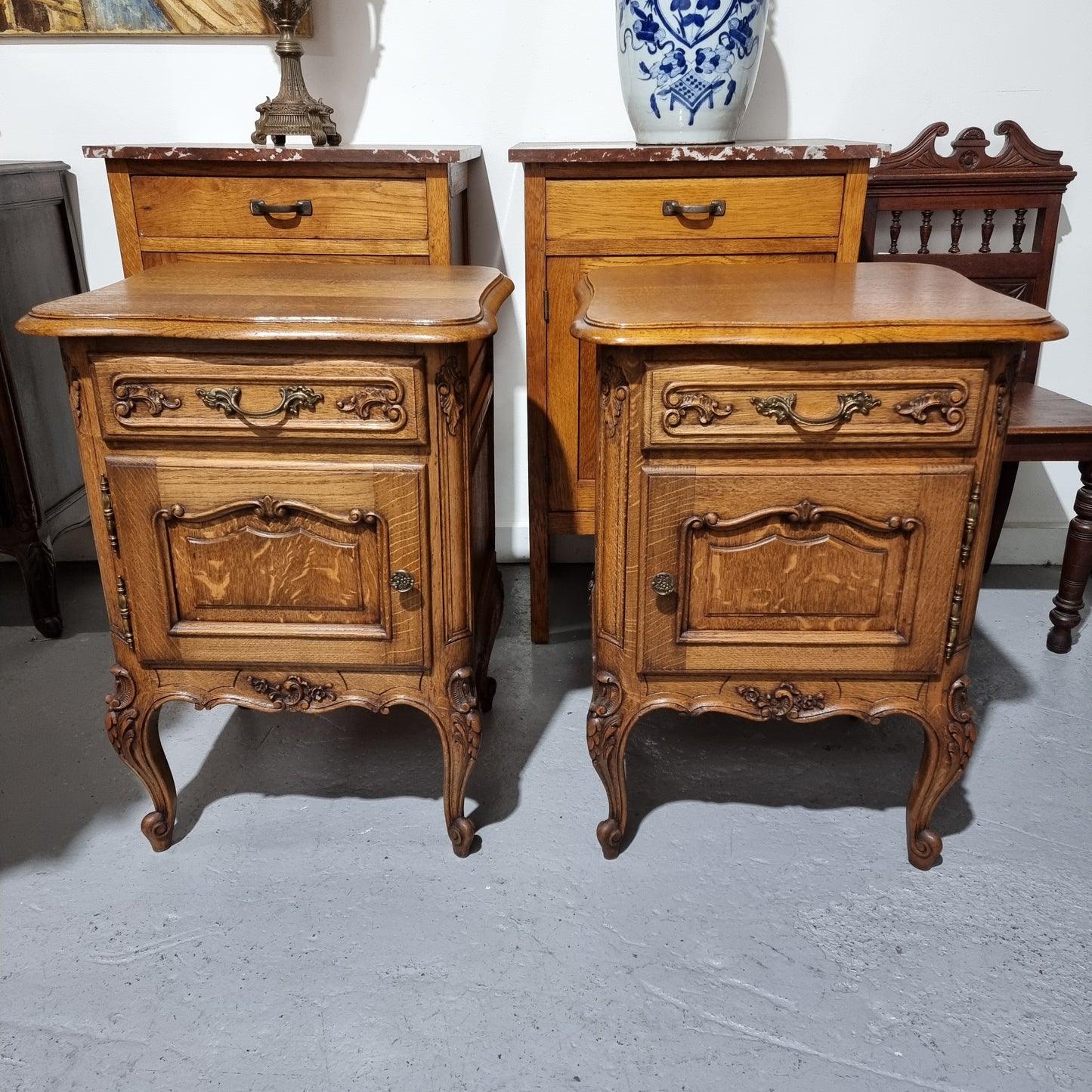 A Rare pair of Antique French Oak Louis XV style wooden top bedside cabinets. Featuring decorative carvings and classical Louis XV cabriole legs. These have been sourced directly from France and are in good original detailed condition.