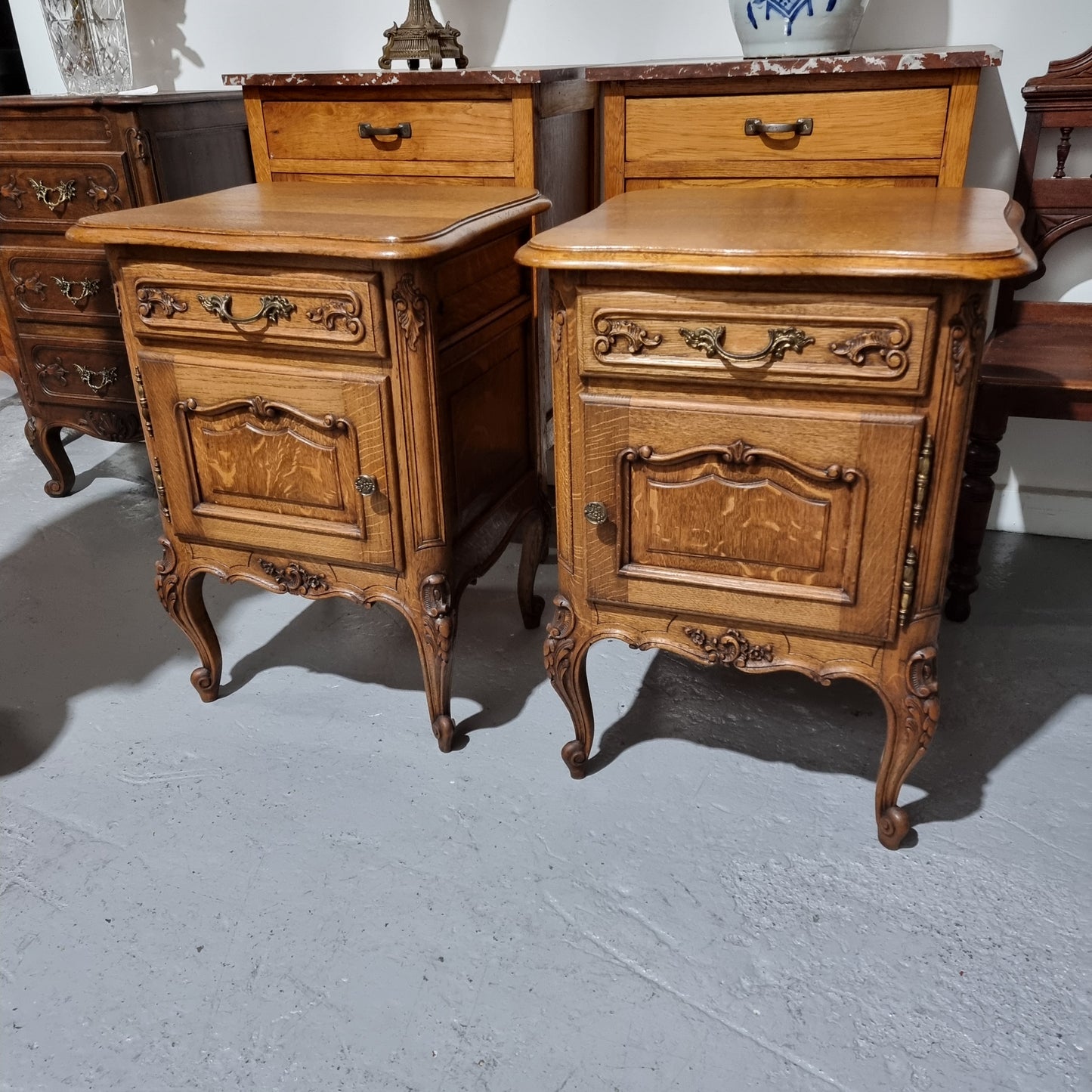 A Rare pair of Antique French Oak Louis XV style wooden top bedside cabinets. Featuring decorative carvings and classical Louis XV cabriole legs. These have been sourced directly from France and are in good original detailed condition.