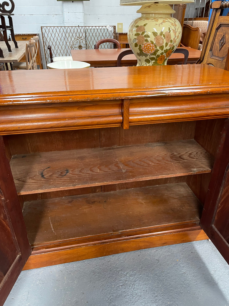 Cedar cupboard / side cabinet with two drawers above a pair of figured paneled doors, decorated with two corbels and on a plinth base. In good original condition and sourced locally.