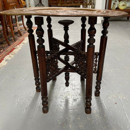 Middle eastern carved folding bases coffee table. It has a copper top intricately pierced and patterned. It is in good original condition. Please see photos as they form part of the description and condition.