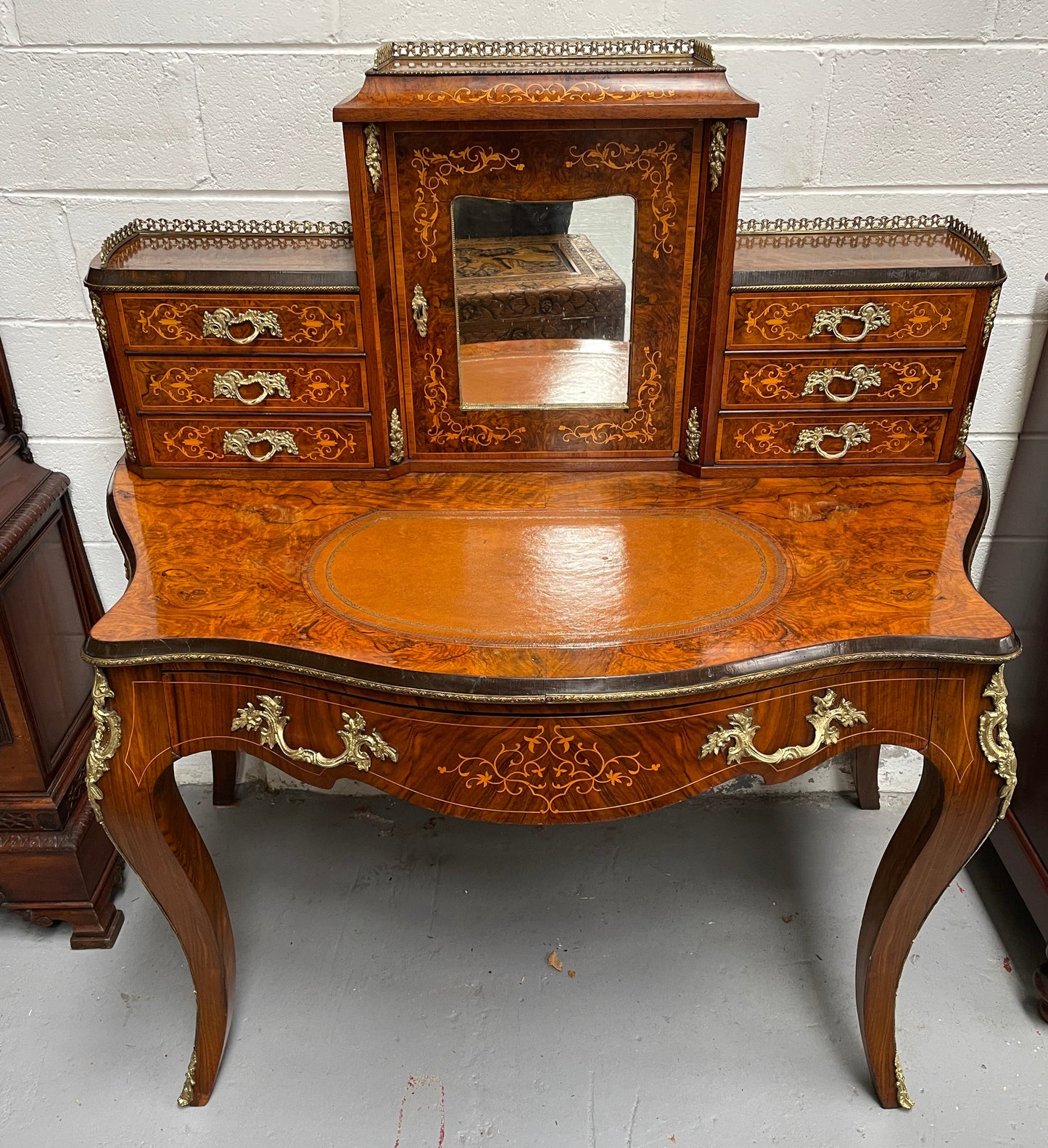 A very attractive burr walnut writing desk (Bonheur De Jour) with ormolu mounts throughout. The boxwood inlaid decoration is featured on the drawers and the mirrored cupboard which also feature brass galleries. The table area features burr walnut and a tooled leather inlay. A long drawer underneath features further inlay and stringing and all have lovely ormolu handles. It is a stunning piece of furniture of fantastic quality and makes a good ladies writing desk. In very good condition.