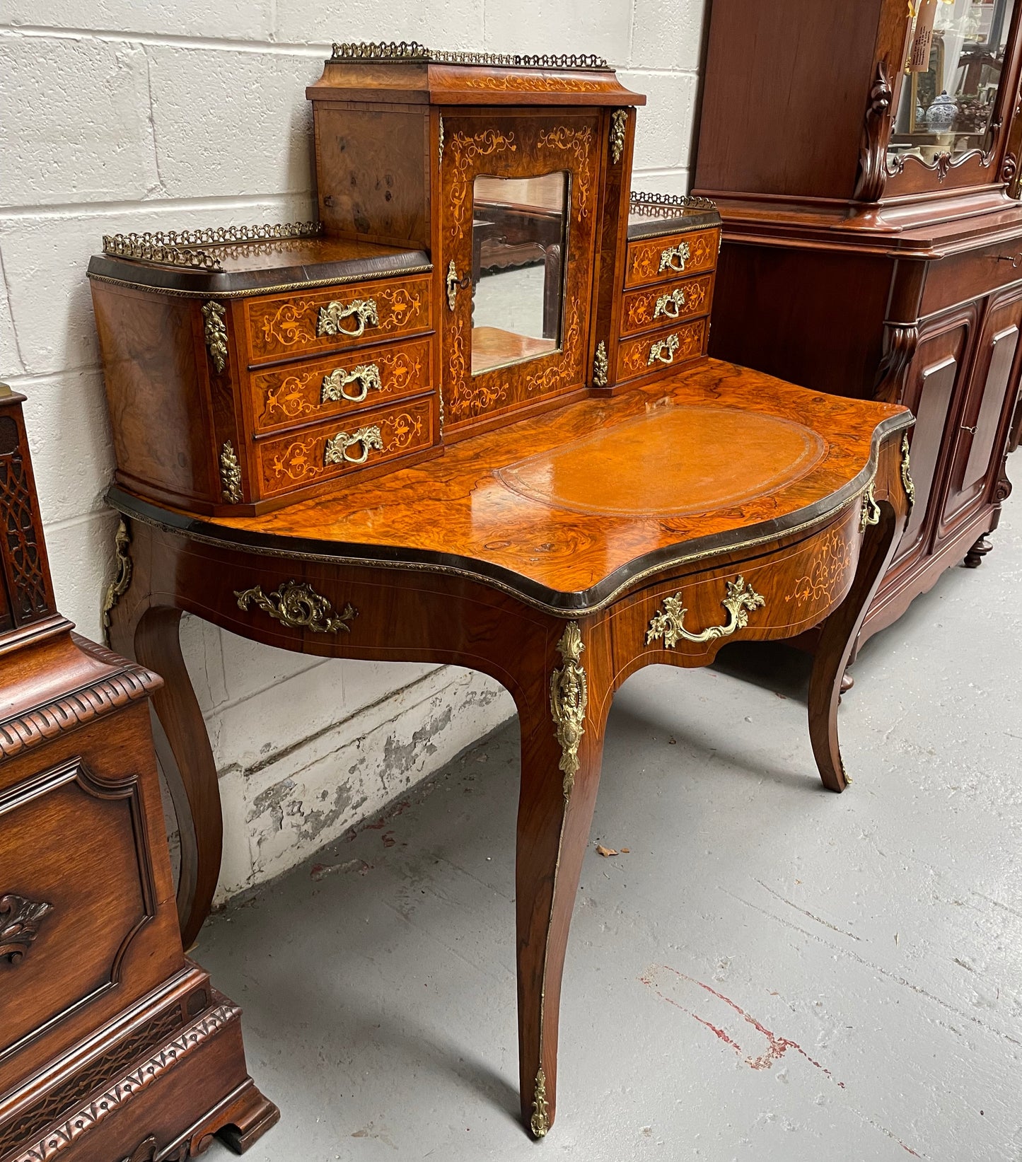 A very attractive burr walnut writing desk (Bonheur De Jour) with ormolu mounts throughout. The boxwood inlaid decoration is featured on the drawers and the mirrored cupboard which also feature brass galleries. The table area features burr walnut and a tooled leather inlay. A long drawer underneath features further inlay and stringing and all have lovely ormolu handles. It is a stunning piece of furniture of fantastic quality and makes a good ladies writing desk. In very good condition.