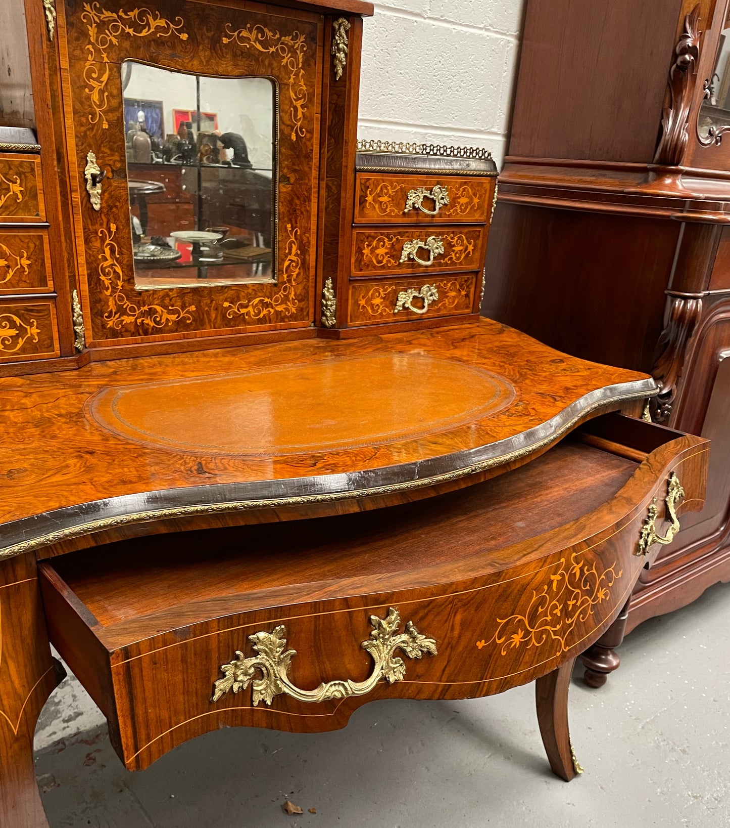 A very attractive burr walnut writing desk (Bonheur De Jour) with ormolu mounts throughout. The boxwood inlaid decoration is featured on the drawers and the mirrored cupboard which also feature brass galleries. The table area features burr walnut and a tooled leather inlay. A long drawer underneath features further inlay and stringing and all have lovely ormolu handles. It is a stunning piece of furniture of fantastic quality and makes a good ladies writing desk. In very good condition.