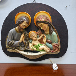 Full view of vintage illuminated Holy Family wall plaque on timber backboard