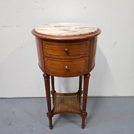 Charming Louis XVI style round side table. Features two drawers, fitted marble top and fluted legs connected by a cane shelf. Sourced directly from France and is in good original&nbsp; detailed condition.