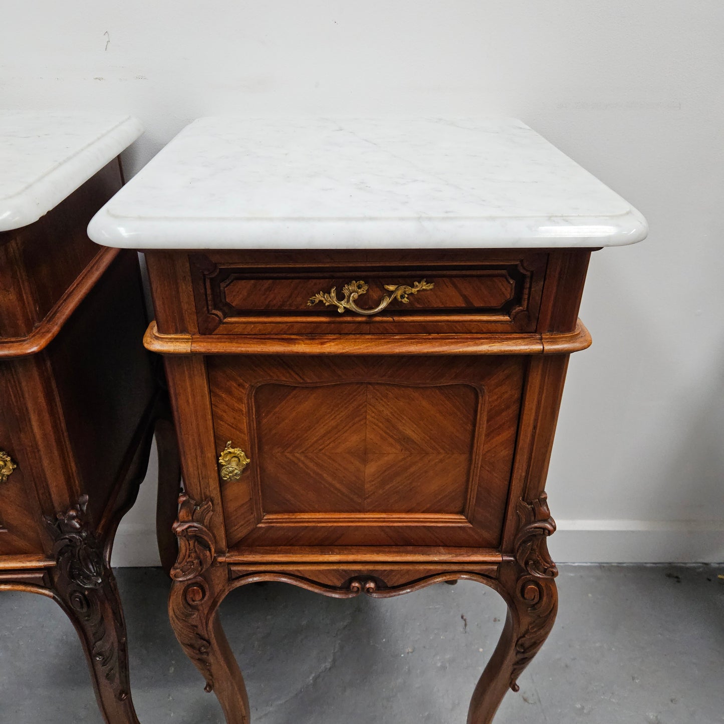 Pair of French Walnut Louis XV Style white marble top bedside cabinets. Featuring beautiful parquetry work and decorative carvings throughout. Sourced directly from France and in good original detailed condition.