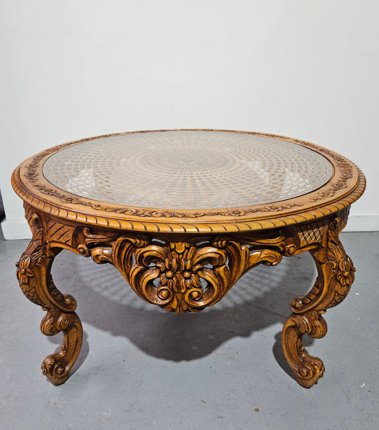 French oak Louis XV style round cane insert coffee table with highly decorative legs and table top. It has a glass cover to fit over the cane. It is in good original condition and has been sourced from France.