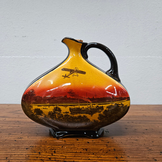 Rare Royal Doulton Dewar's whisky jug pattern number 150, in brown red and yellow glaze, one side with&nbsp;transfer&nbsp;printed scene depicting the Bleriot monoplane flown by Maurice Guillaux over Sydney harbour in 1914, the other side lettered Dewar's, marked on the bottom with the Royal Doulton Logo and '150 RdNo 636615', 16.5 cm high.&nbsp; There is some crazing on the item.&nbsp;&nbsp;