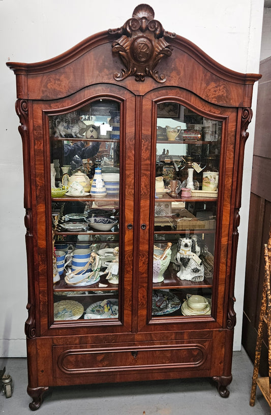 Wooden display cabinet with glass doors filled with decorative items against a white wall.