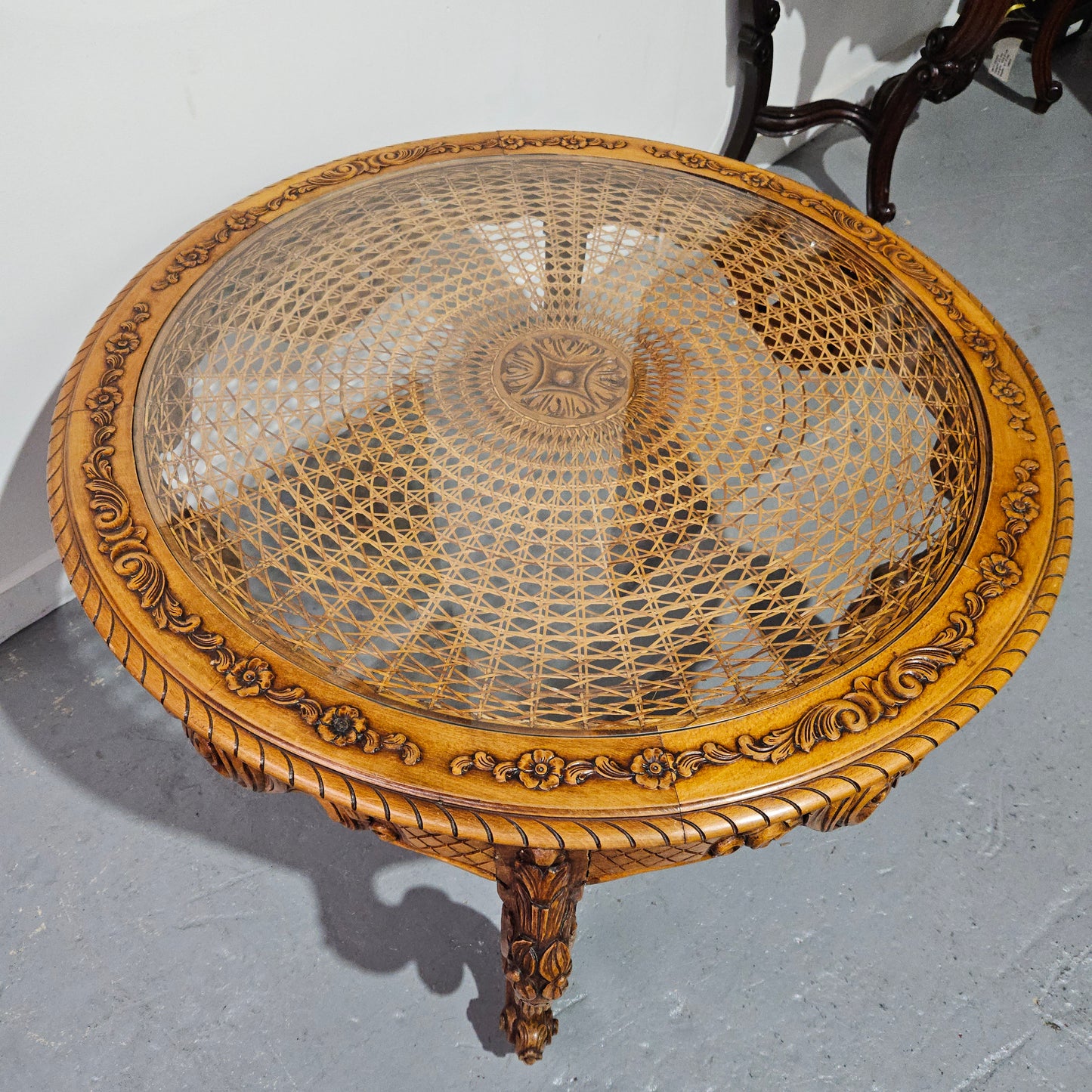French oak Louis XV style round cane insert coffee table with highly decorative legs and table top. It has a glass cover to fit over the cane. It is in good original condition and has been sourced from France.