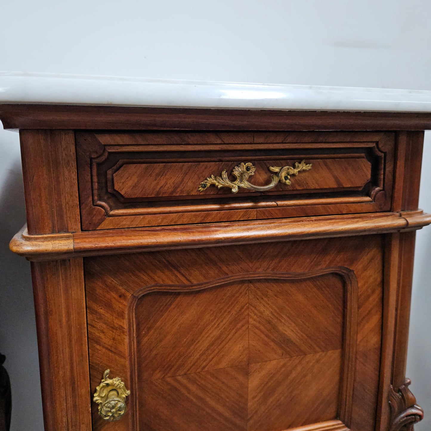 Pair of French Walnut Louis XV Style white marble top bedside cabinets. Featuring beautiful parquetry work and decorative carvings throughout. Sourced directly from France and in good original detailed condition.