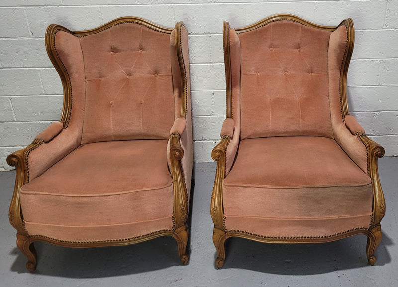 French pair of  Walnut Louis XV style pink upholstered wing back chairs. They are very comfortable to sit in and are of generous portions. The fabric is in good original condition and does have stains and would ideally be reupholstered.