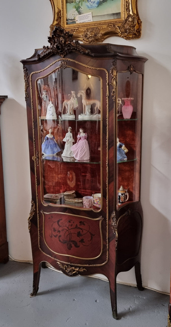 French Louis XV style marquetry inlaid vitrine with ormolu mounts and curved glass. The inside in lined with a red velvet upholstery and has two glass shelves. It has been sourced from France and is in good original detailed condition.