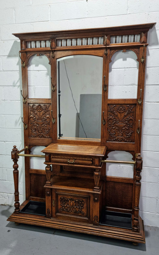 Grand Henry 2nd Style French Oak hall stand with 12 hanging hooks. Also has one cupboard and drawer for storage along with a mirror and two areas either side for umbrellas and walking sticks. In good original detailed condition.