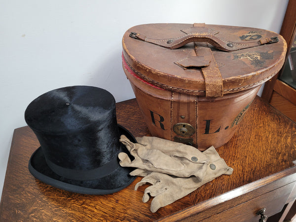 Black Silk Top Hat manufactured by the Buzolich Family, Melbourne between 1910 – 1927 (now City Hatters Flinders Street). Includes original Leather Hat Box with insert for hat. Hat in good condition, box shows wear and deterioration commensurate with age and has part labels from travel affixed.