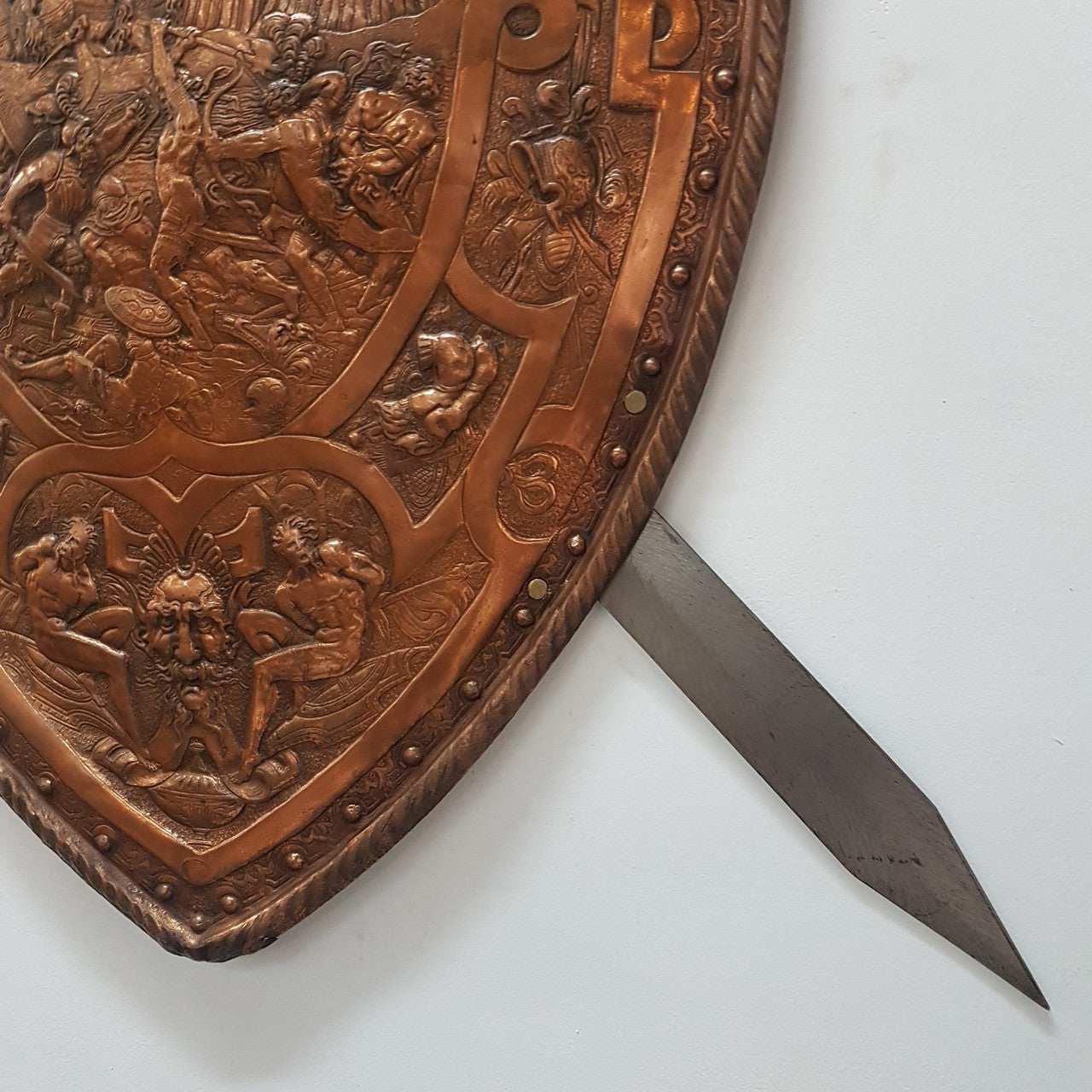 A beautiful European Antique highly detailed embossed copper shield with swords. Look closely to see the amazing detail in the shield of a fighting scene. It has brass handles on the steel swords. Is in good original condition with a slight crack (see photo).