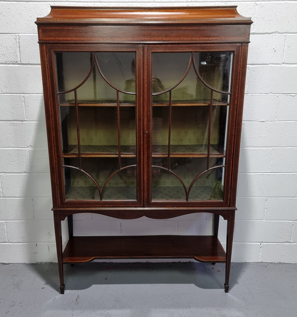 Edwardian Sheraton Revival Mahogany display cabinet with green upholstered  fabric backing and shelving with inlay and two decorative glazed doors.
