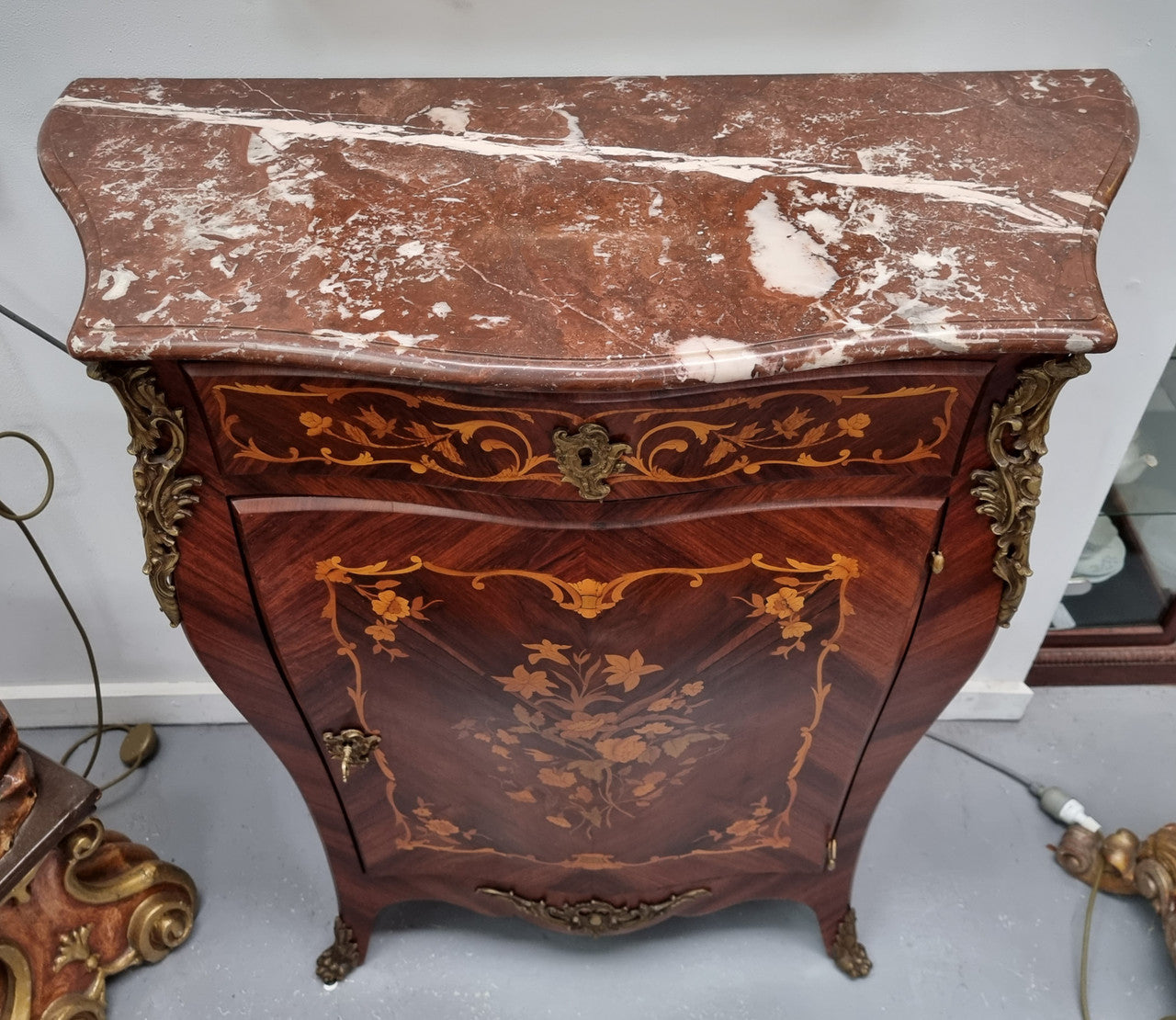 Stunning French Transitional style Mahogany marquetry inlay salon cabinet in the bombe shape. It has one draw, one shelf, marble top & ormolu decoration. Sourced from France and in good original detailed condition.